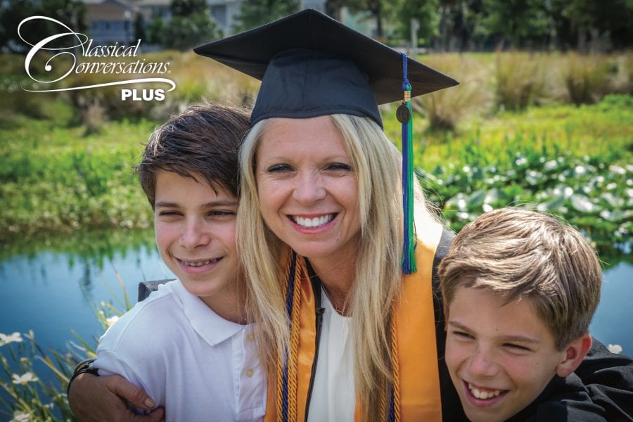 a homeschool mom dressed in graduation regalia hugs her two boys and smiles at the camera